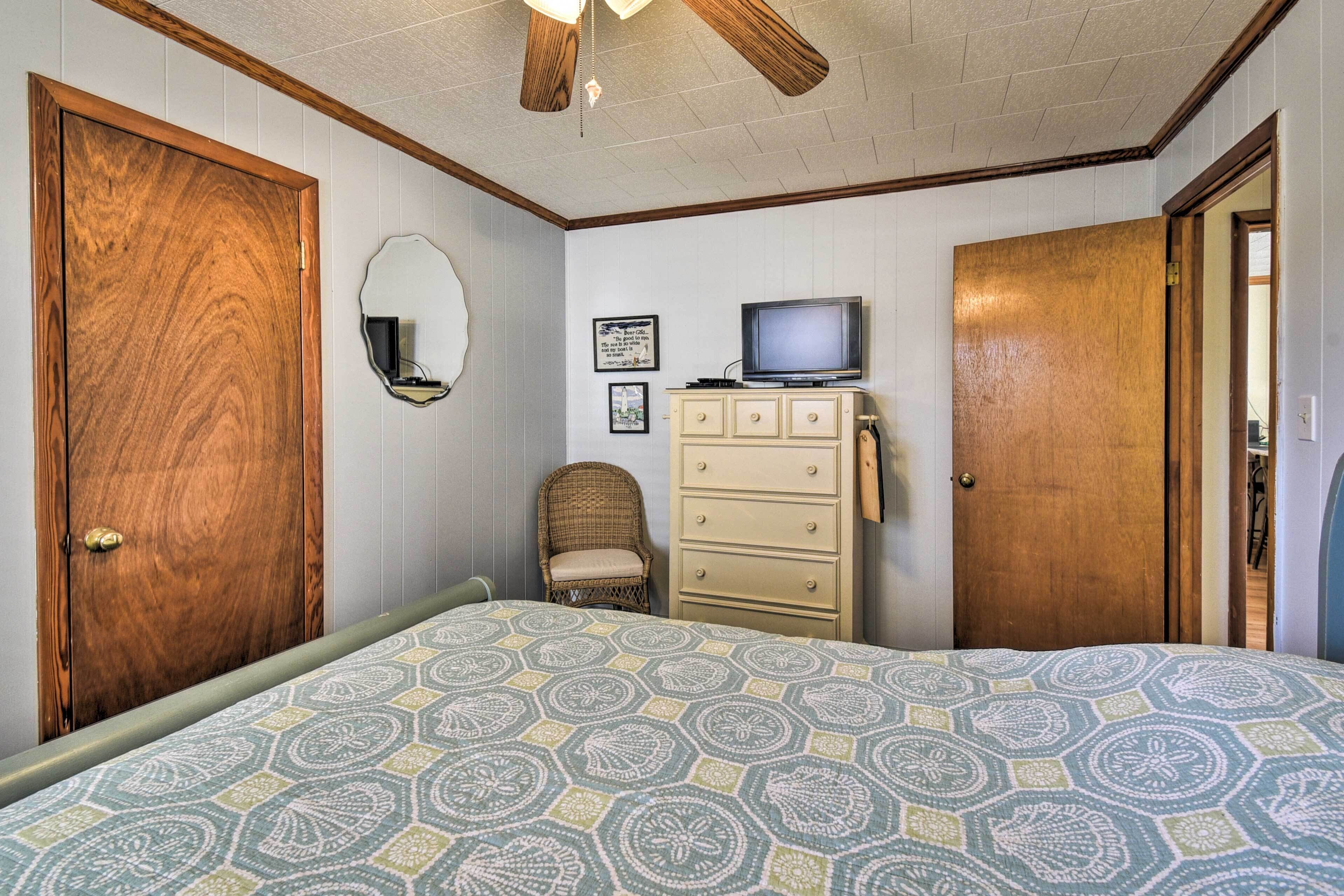A bedroom with a bed, dresser, television, and two doors.