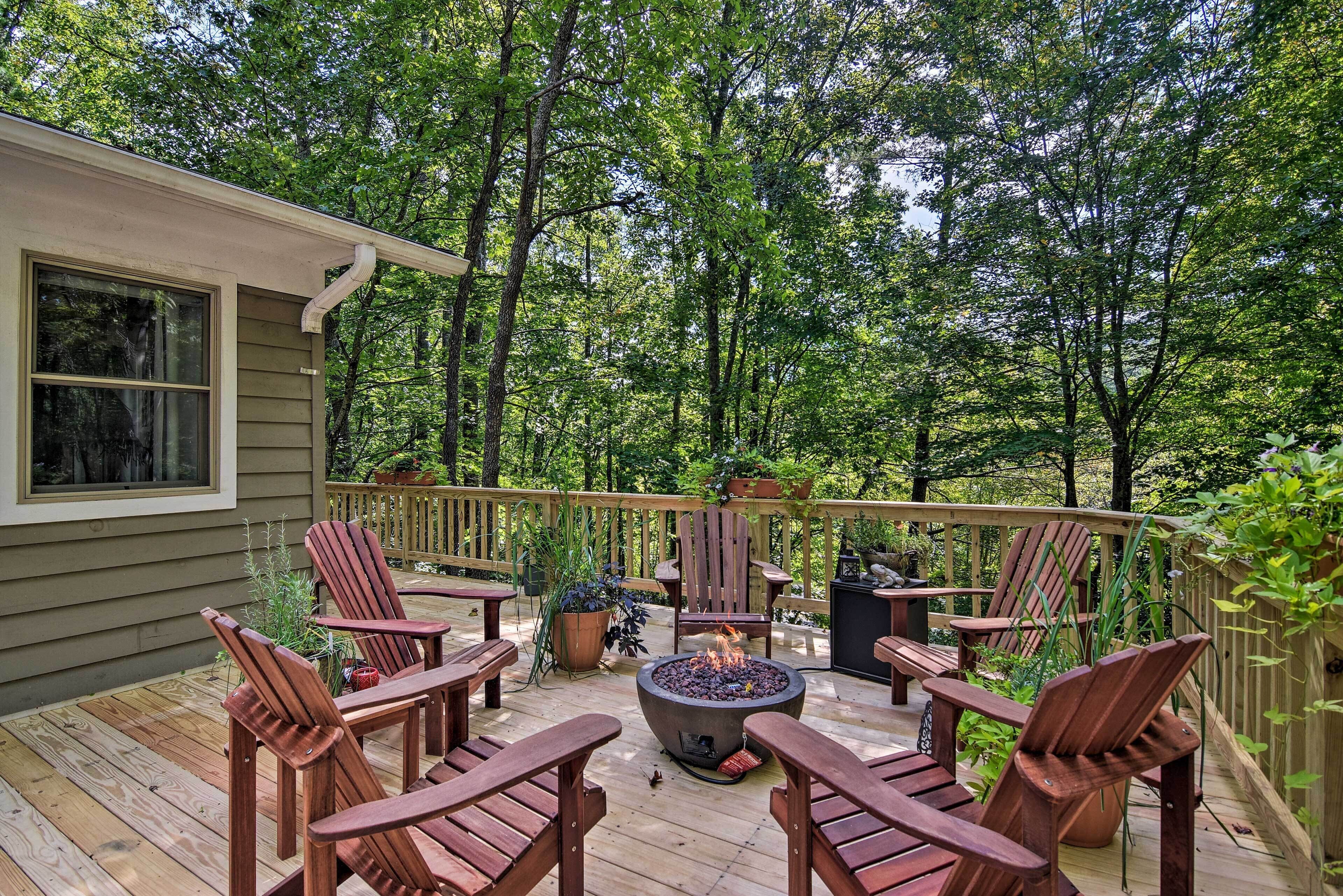 A wooden deck with Adirondack chairs and a fire pit, surrounded by lush greenery.