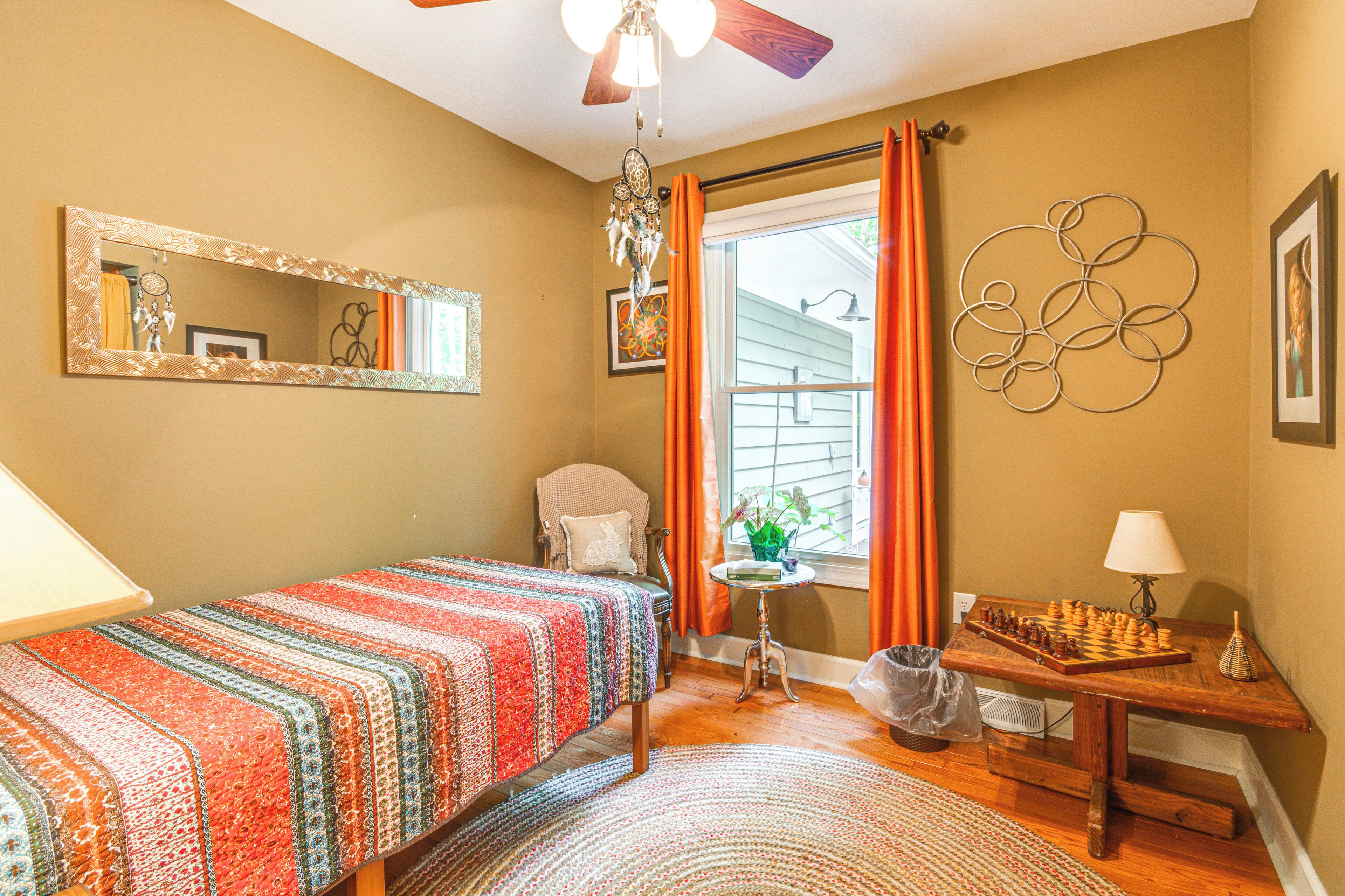 A bedroom with a bed, a chair, a window with curtains, a chessboard, and a wall with a circular design.