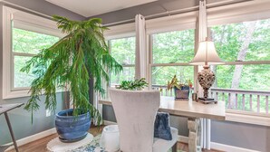 A room with a large window, a potted plant, a chair, a table with a lamp, and a view of trees. - Cozy Hideaway w/ Grill, 17 Mi to Asheville (Black Mountain)