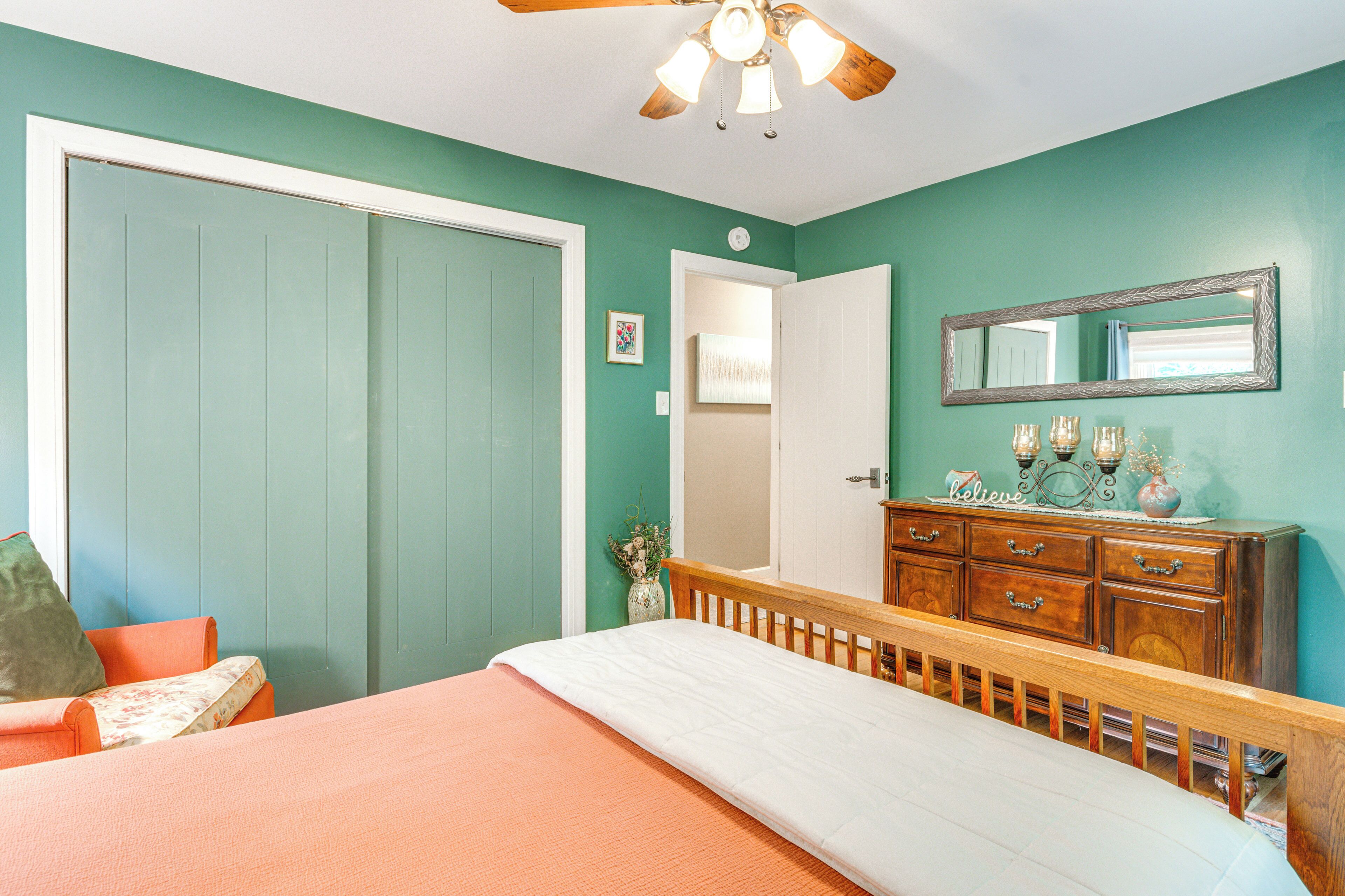 A bedroom with teal walls, a wooden bed frame, a dresser, and a ceiling fan.