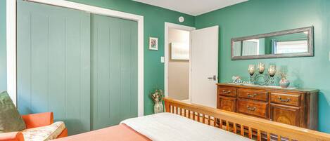 A bedroom with teal walls, a wooden bed frame, a dresser, and a ceiling fan.