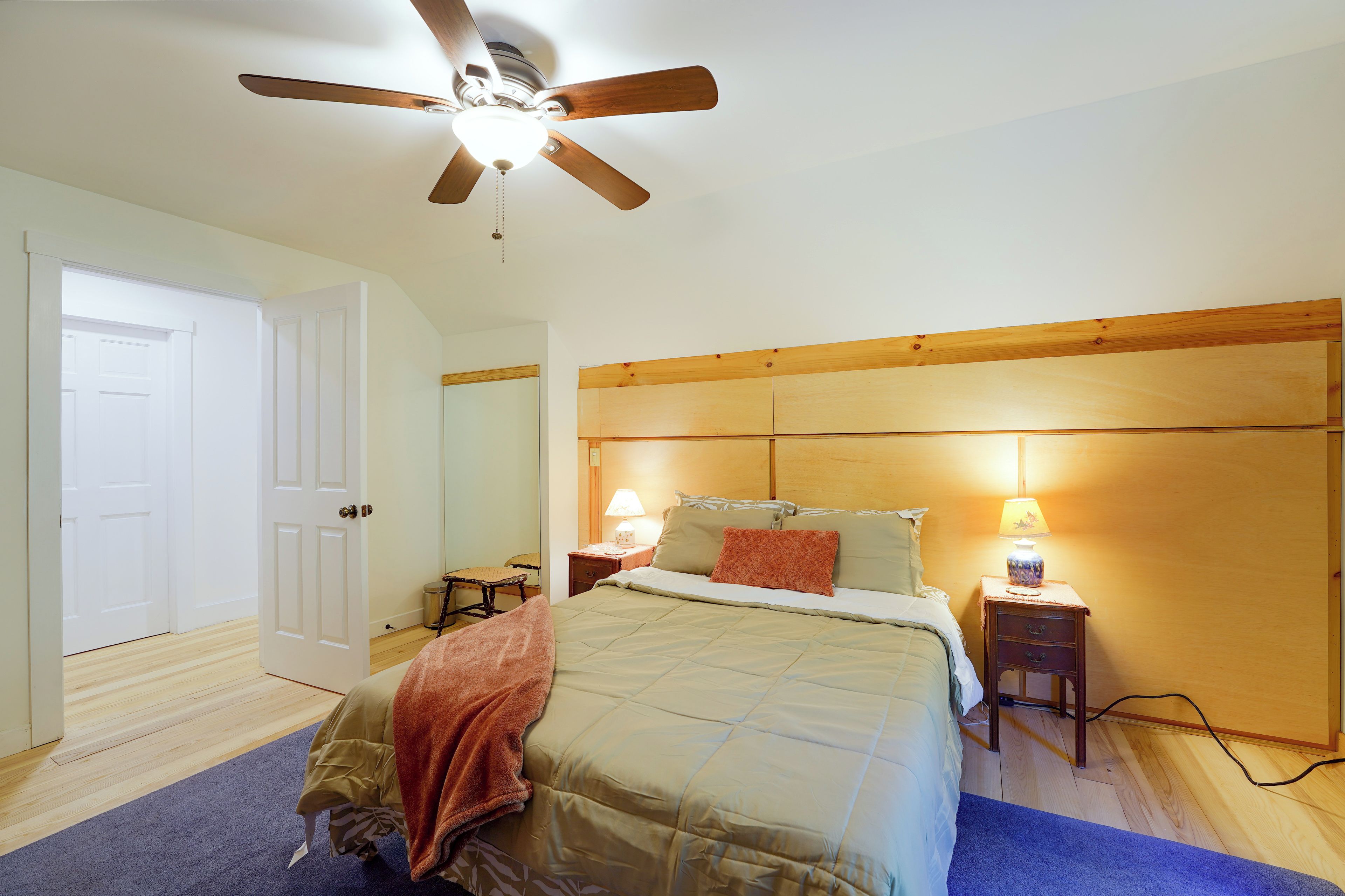 Une chambre à coucher avec un lit, des lampes de chevet, une tête de lit en bois, un ventilateur de plafond et une porte.