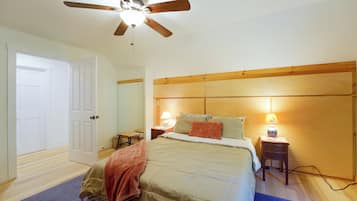 A bedroom with a bed, bedside lamps, a wooden headboard, a ceiling fan, and a door.