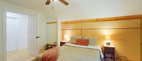 Une chambre à coucher avec un lit, des lampes de chevet, une tête de lit en bois, un ventilateur de plafond et une porte.