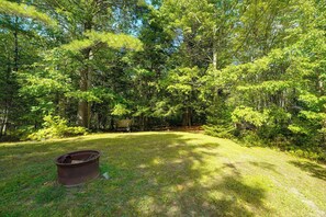 A forested area with a grassy clearing, a rusty boat, and a wooden fence.