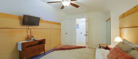 A bedroom with a bed, a ceiling fan, a TV, a dresser, and a door leading to another room.