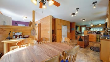 A wooden interior with a dining table, chairs, a kitchen area, and a ceiling fan.