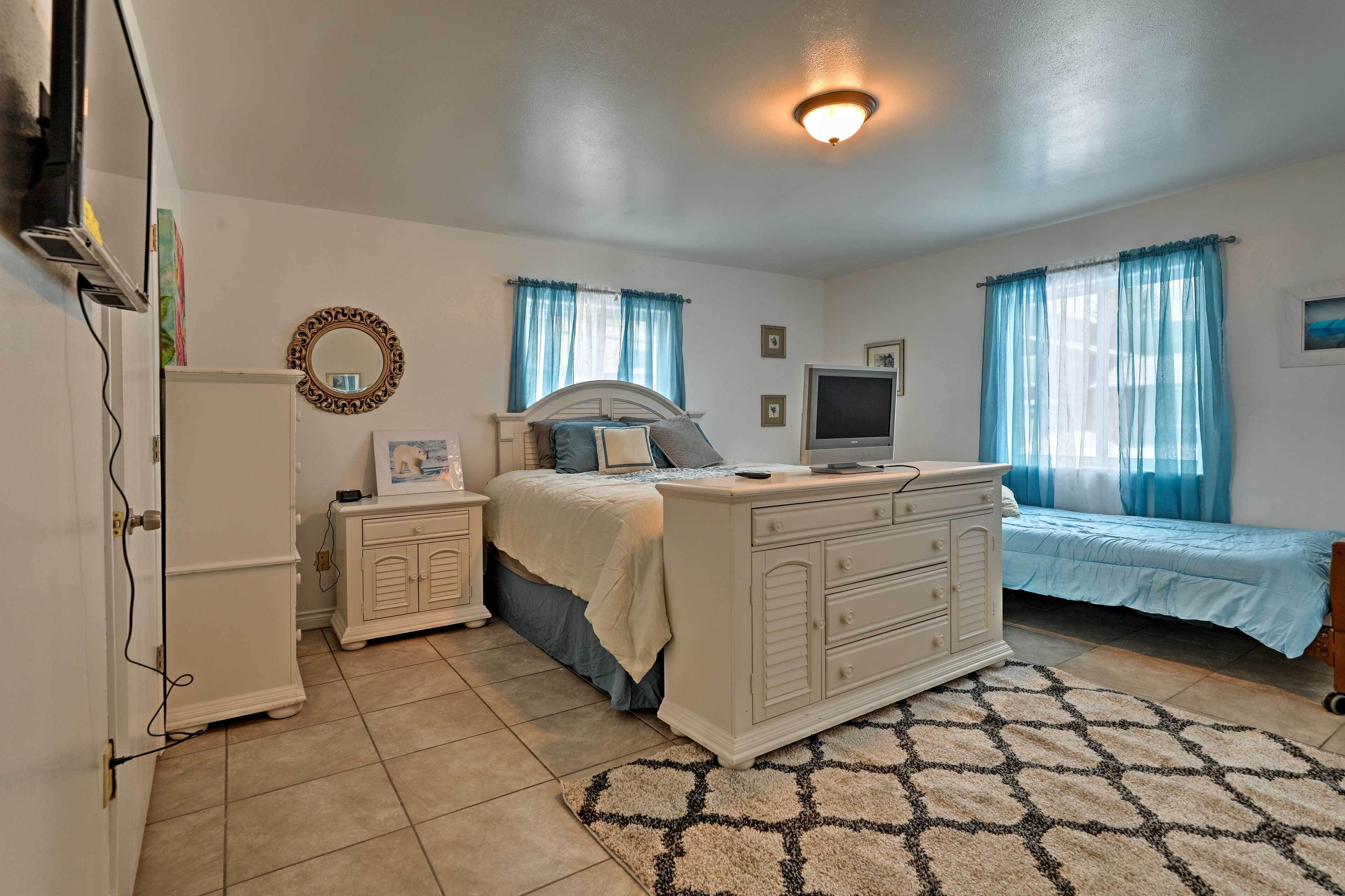 A bedroom with a bed, dresser, TV, and a mirror on the wall.