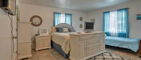 A bedroom with a bed, dresser, TV, and a mirror on the wall.