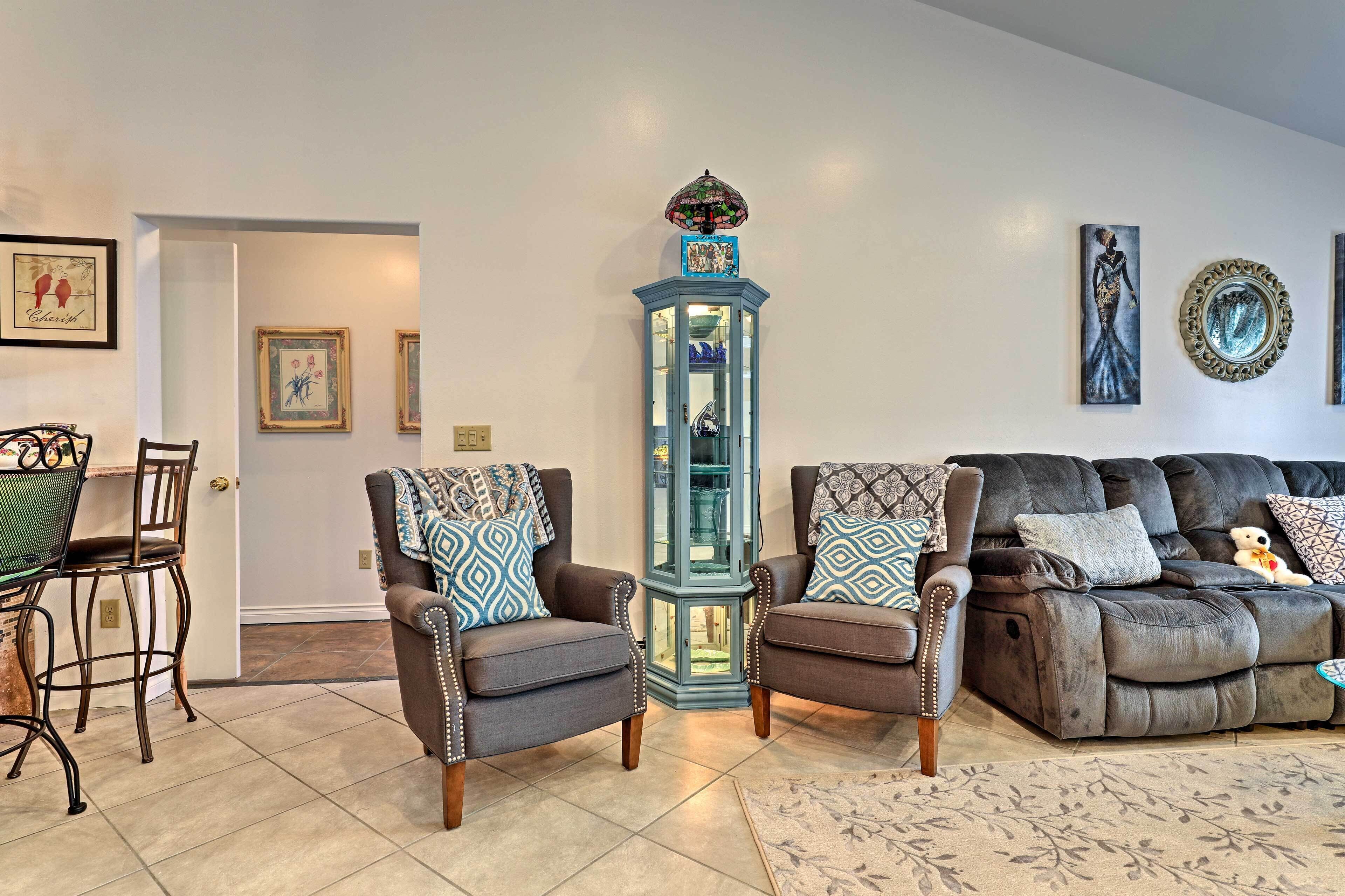 A living room with two armchairs, a glass cabinet, and a sofa with decorative pillows.