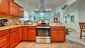A kitchen with wooden cabinets, a stainless steel range hood, a red kettle, and a large island. - Expansive Getaway ~ 2 Miles to Mendenhall Glacier! (Juneau)