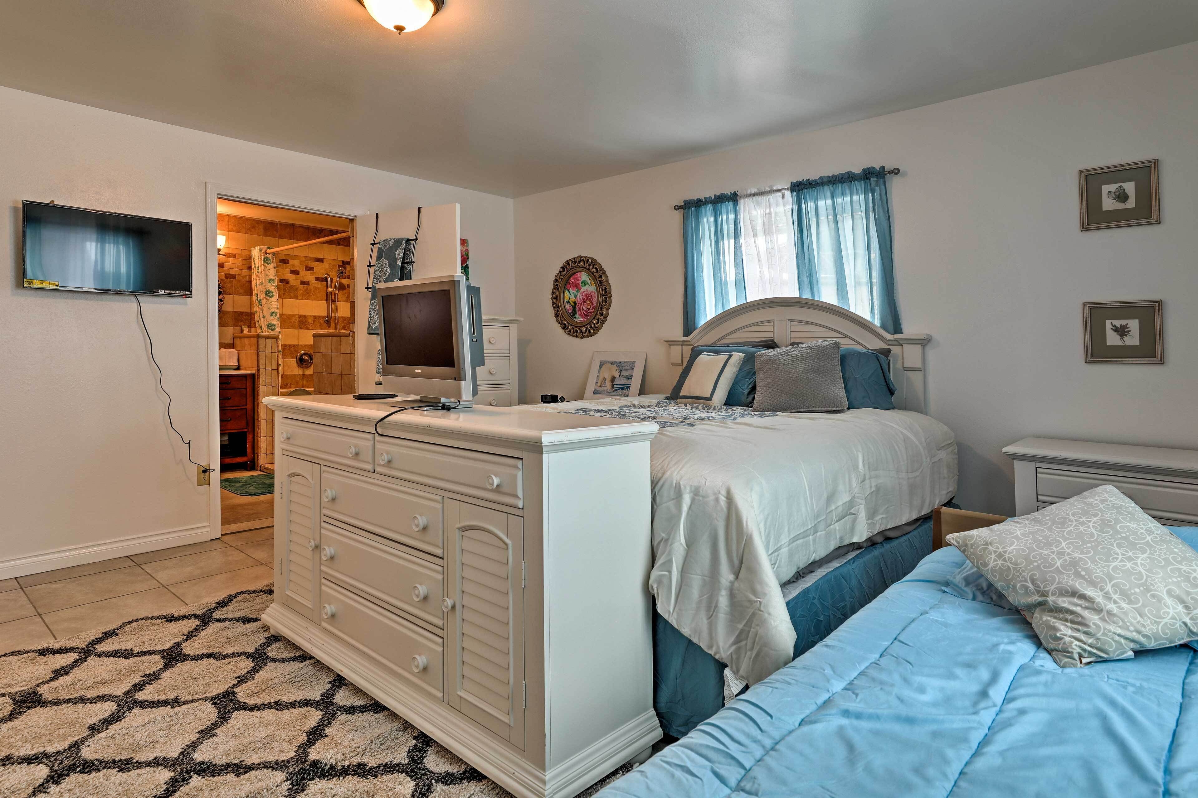 Un dormitorio con cama, cómoda, televisor y baño visible a través de una puerta abierta.