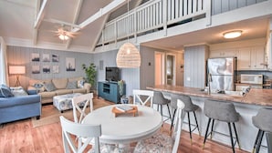 Een ruime woonkamer met hoge plafonds, een balkon, een keuken met een roestvrijstalen koelkast en een eethoek met witte stoelen en een ronde tafel.