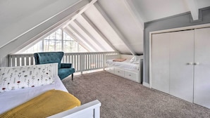 Een slaapkamer met een schuine daklijn, een bed met een wit hoofdbord, een blauwe stoel, een witte kast en een raam met uitzicht op bomen.