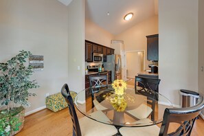 A modern kitchen with dark wooden cabinets, stainless steel appliances, and a glass dining table with a vase of sunflowers.