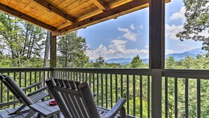 A wooden deck with two lounge chairs and a red plate, overlooking a forested landscape with mountains in the distance. - Gatlinburg Cabin w/ Pool Table & Hot Tub! (Sevierville)