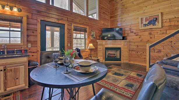 A cozy cabin interior with a dining area, a fireplace, and a television mounted on the wall. - Gatlinburg Cabin w/ Pool Table & Hot Tub! (Sevierville)