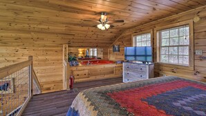 A wooden cabin bedroom with a bed, a television, a small kitchen area, and a staircase leading to a balcony. - Gatlinburg Cabin w/ Pool Table & Hot Tub! (Sevierville)
