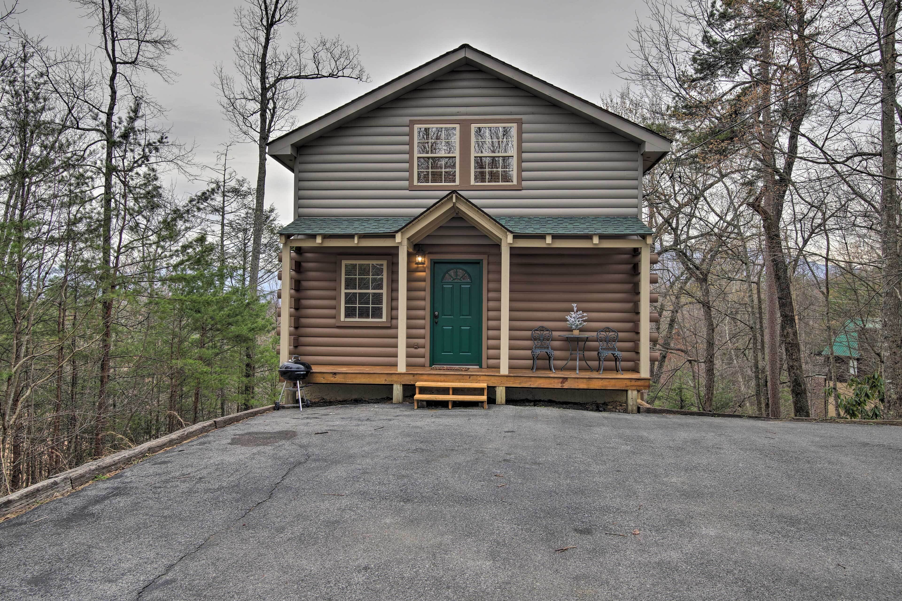 A log cabin with a green door, two windows, and a porch with a bench.