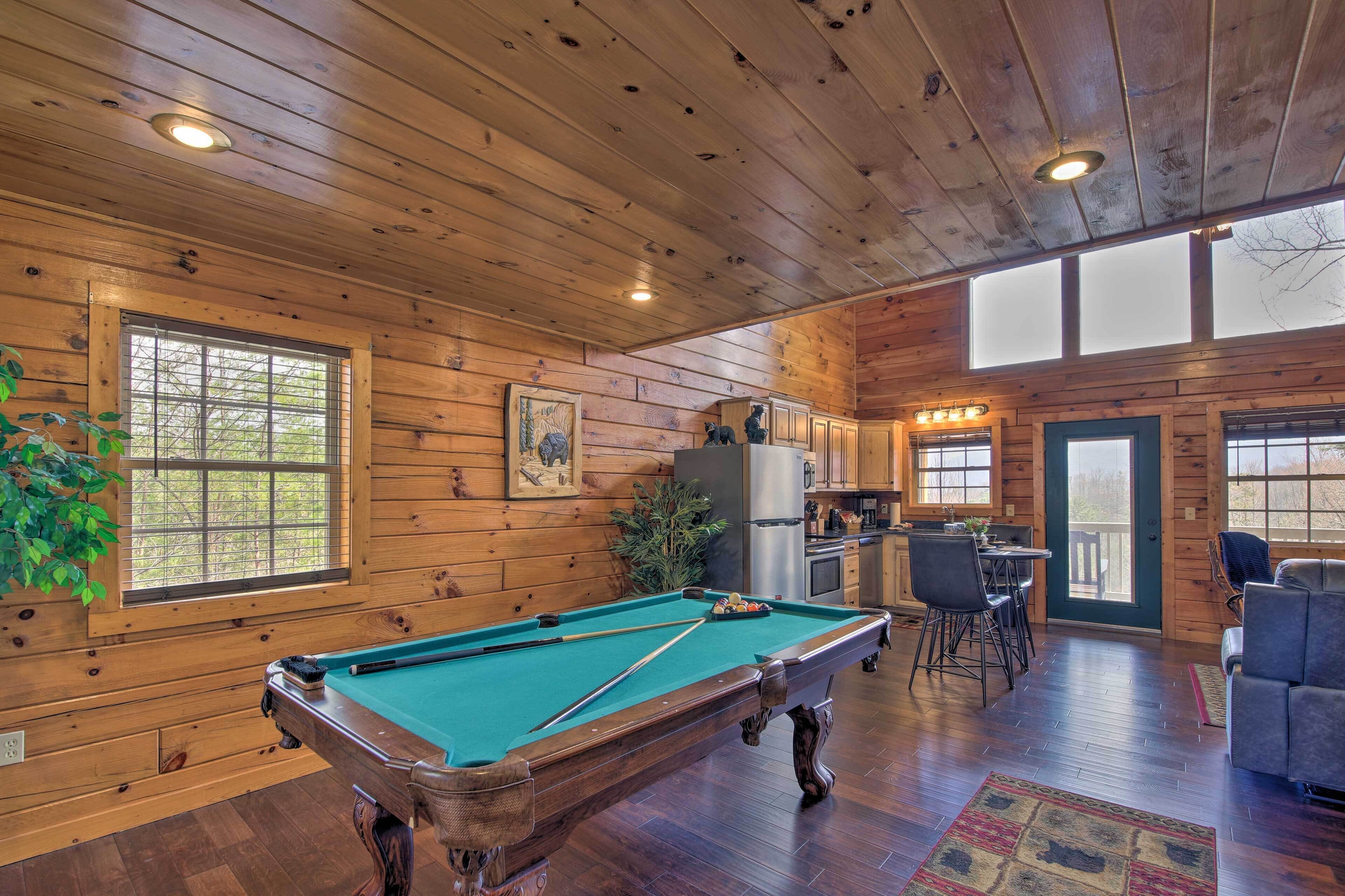 A wooden cabin interior with a pool table, kitchen area, and seating.