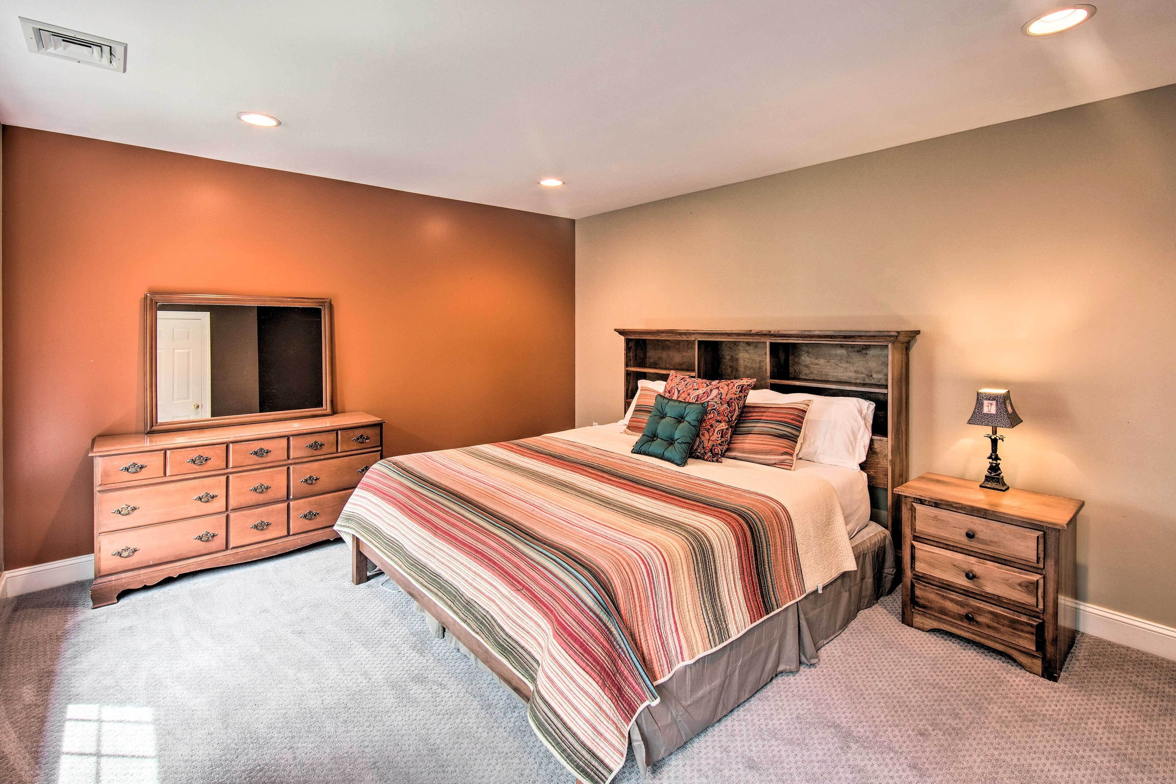 A bedroom with a large bed, a dresser, a nightstand, and a mirror.
