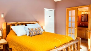 Een bed met houten frame en een gele dekbedovertrek, een witte deur en een houten kast op de achtergrond.