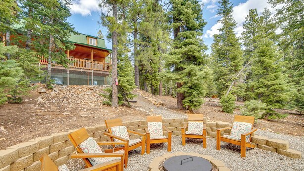 A wooden deck with outdoor seating and a fire pit, surrounded by trees and a building with a green roof. - Duck Creek Village Cabin Near National Forest! (Duck Creek Village)