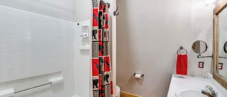 Un baño con una bañera blanca, cortina de ducha con estampado de ciervo, tapete de baño rojo, lavabo blanco y espejo con marco de madera.