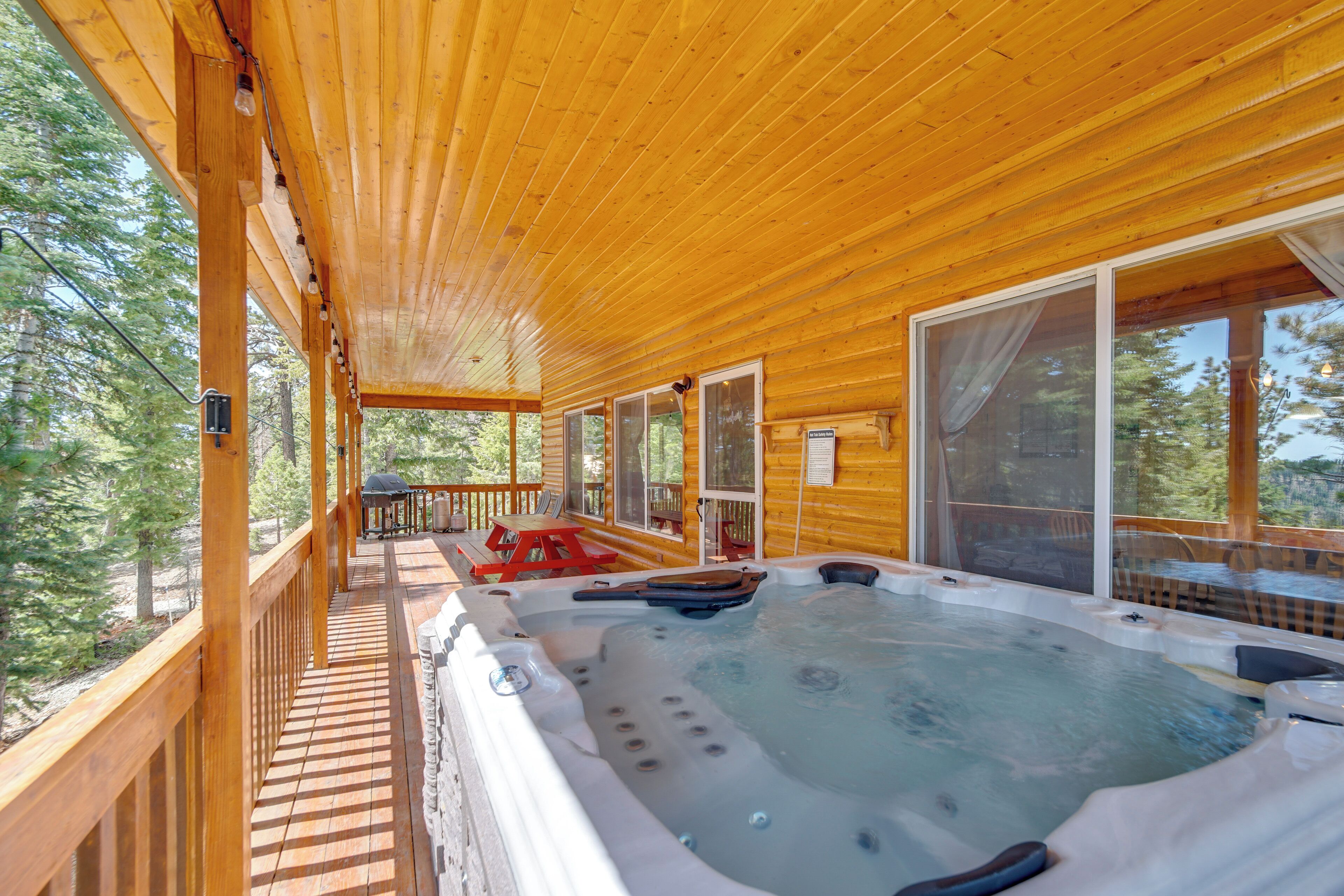 A wooden deck with a hot tub, outdoor seating, and large windows.