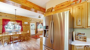 A cabin interior with a large stainless steel refrigerator, wooden dining table with chairs, and a wooden ceiling. - Duck Creek Village Cabin Near National Forest! (Duck Creek Village)