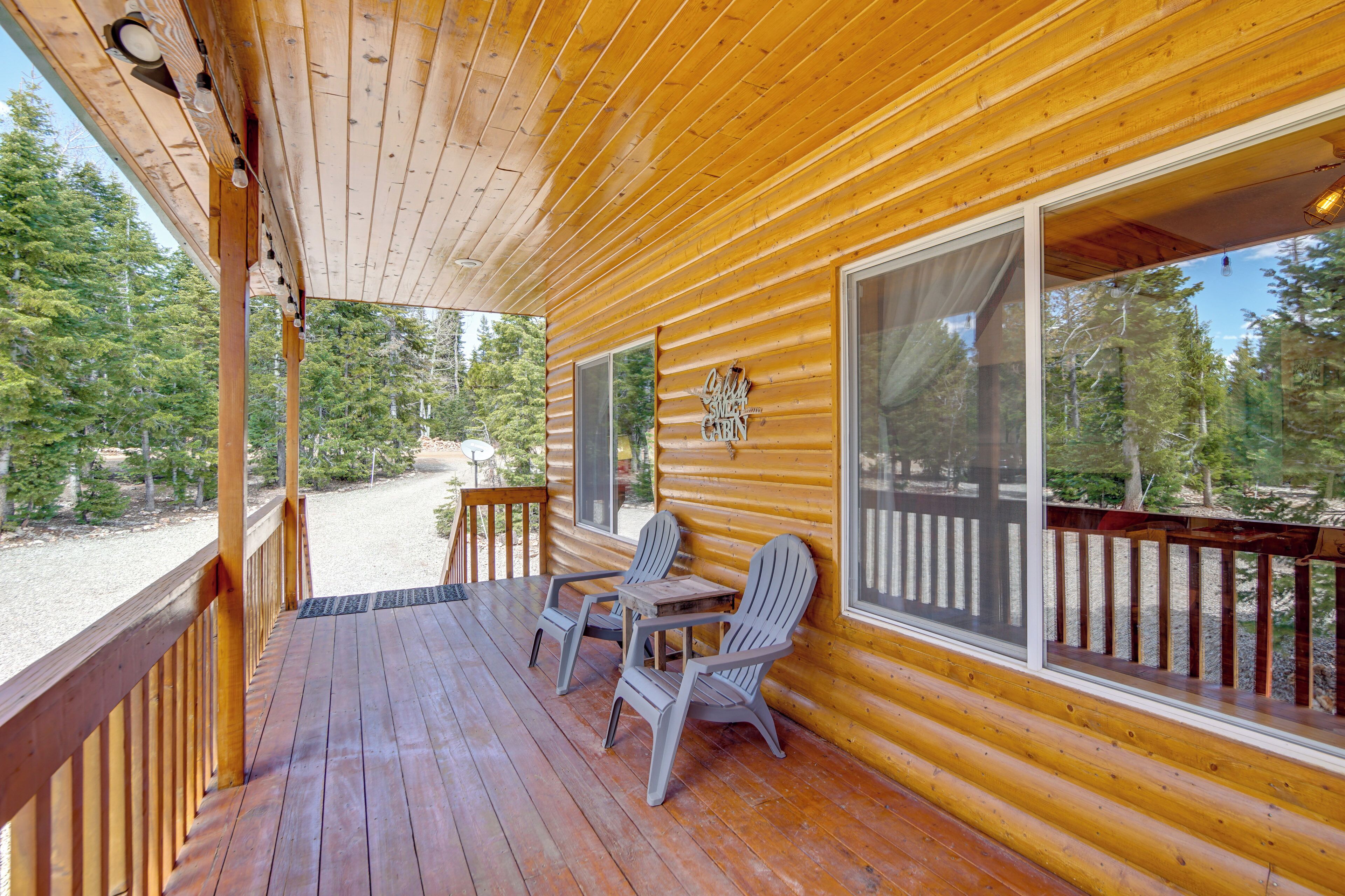 Une terrasse en bois avec des fauteuils Adirondack et une table, donnant sur une zone boisée.
