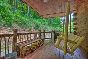 A wooden deck with a hanging chair, a bench, and a grill.