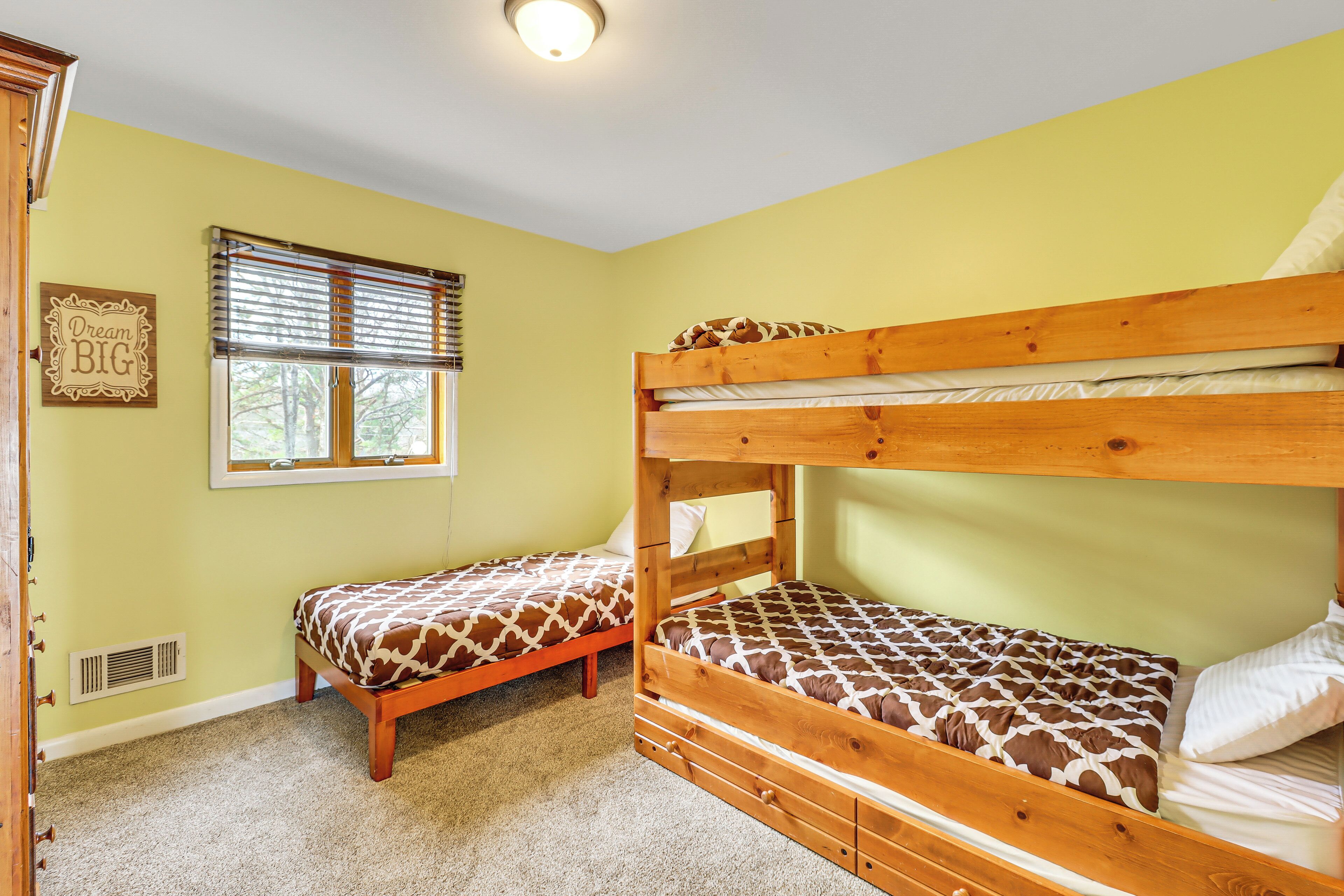 A room with two bunk beds, a window with blinds, a vent, and a wall-mounted sign.