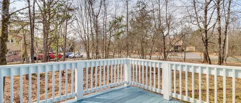 A wooden deck with a white railing, surrounded by leafless trees and a clear sky.