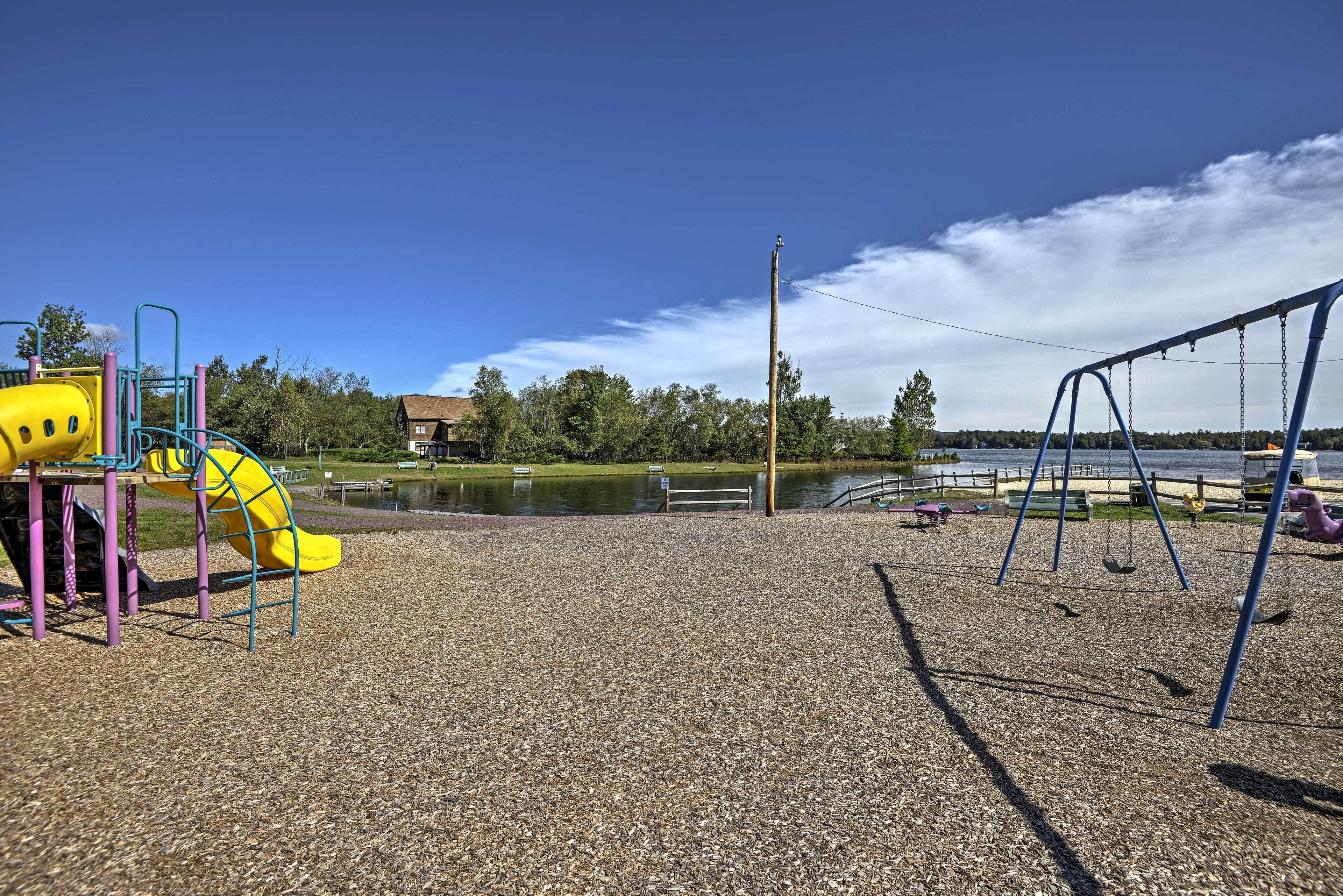 Ein Spielplatz mit Rutsche und Schaukeln, einem Kiesbelag und einem See im Hintergrund.