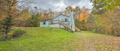 A house with a porch and a staircase leading to the front door, surrounded by trees with autumn leaves.