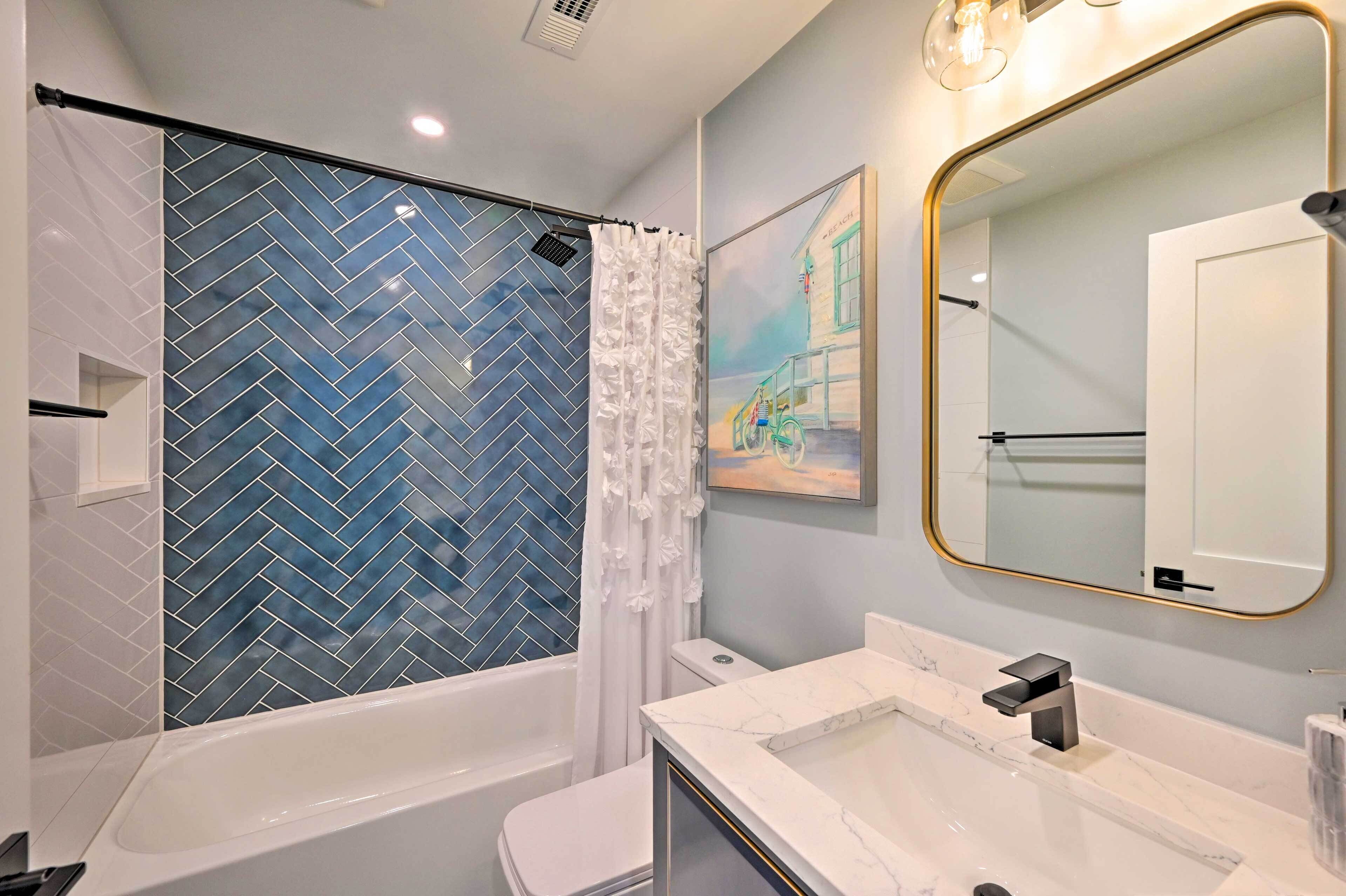 A modern bathroom with a herringbone tile shower, a white toilet, a marble sink, and a large mirror with a gold frame.