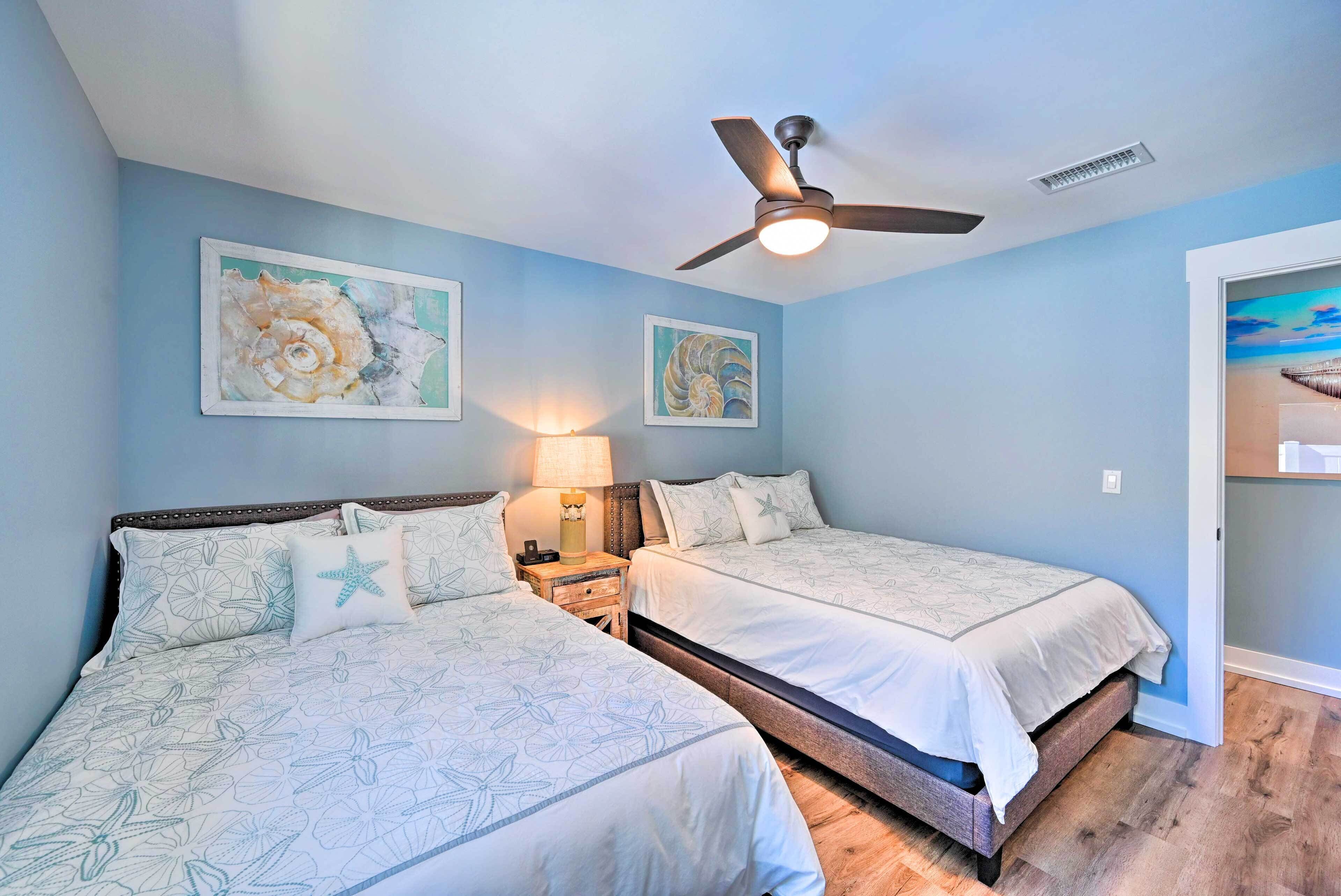 A bedroom with two beds, a ceiling fan, and artwork on the walls.
