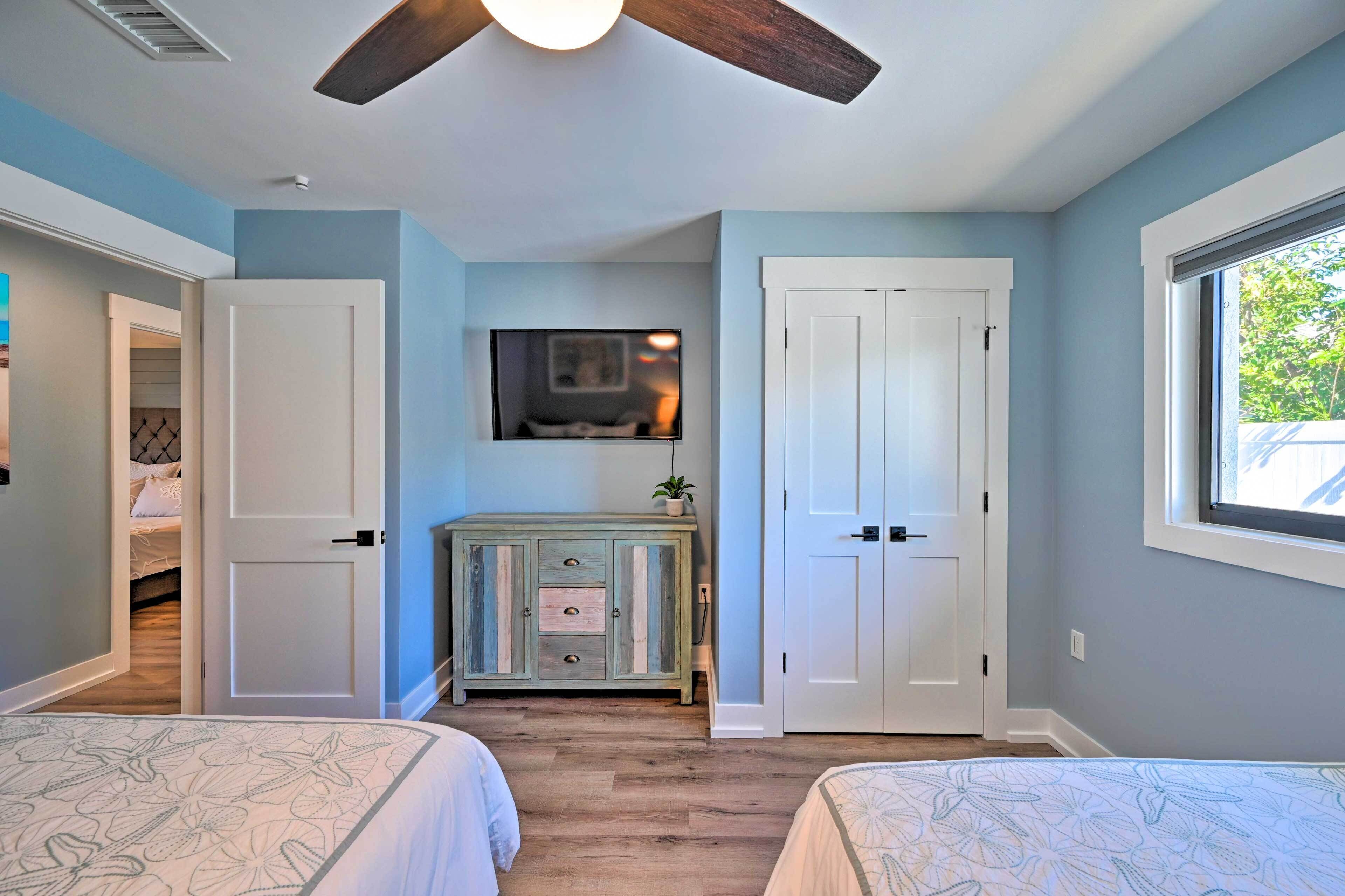 Une chambre avec deux lits, un ventilateur de plafond, un téléviseur fixé au-dessus d’une commode et une fenêtre donnant sur un paysage verdoyant.
