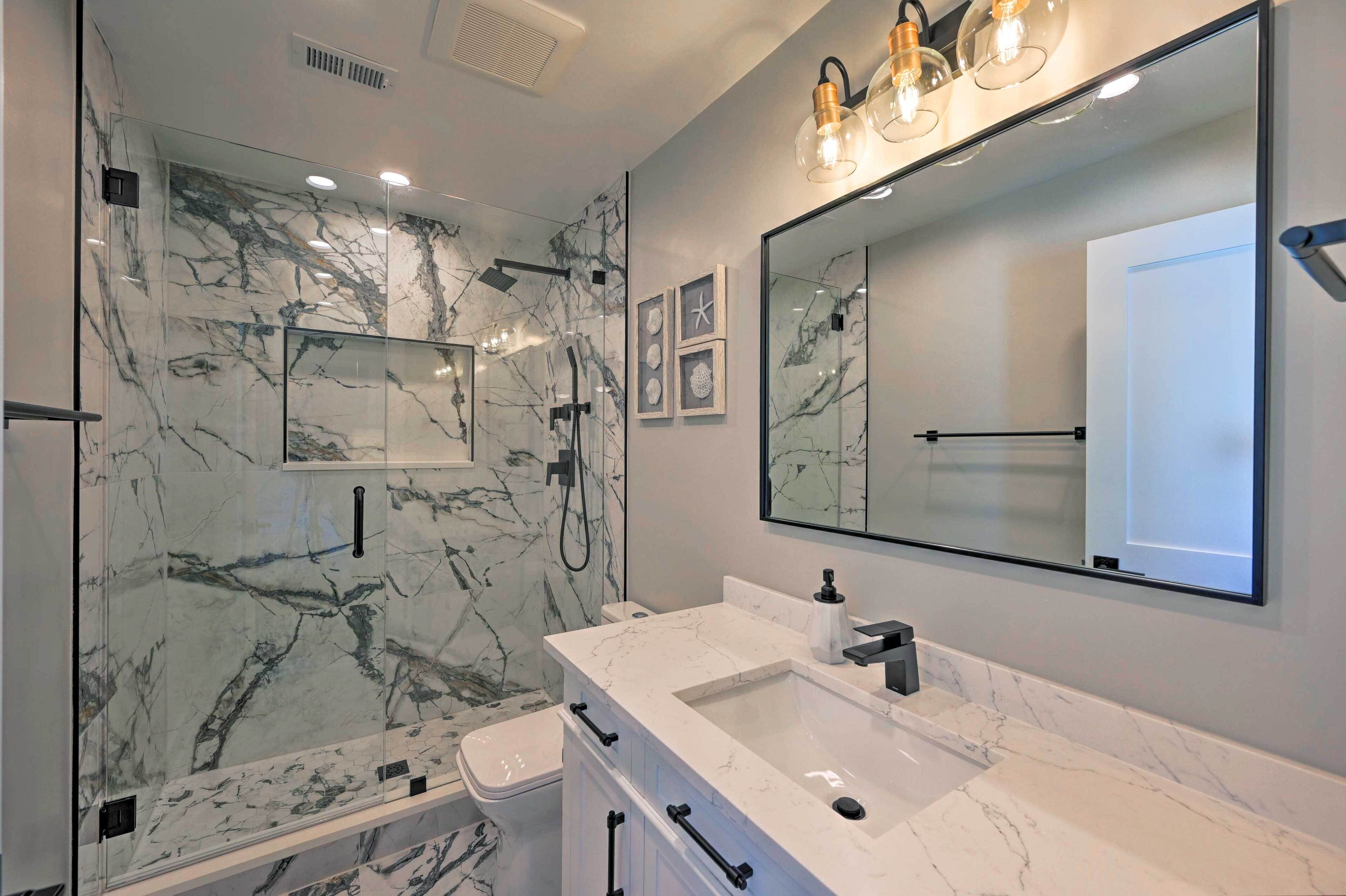 A modern bathroom with a marble shower enclosure, a large mirror, and a white countertop sink.