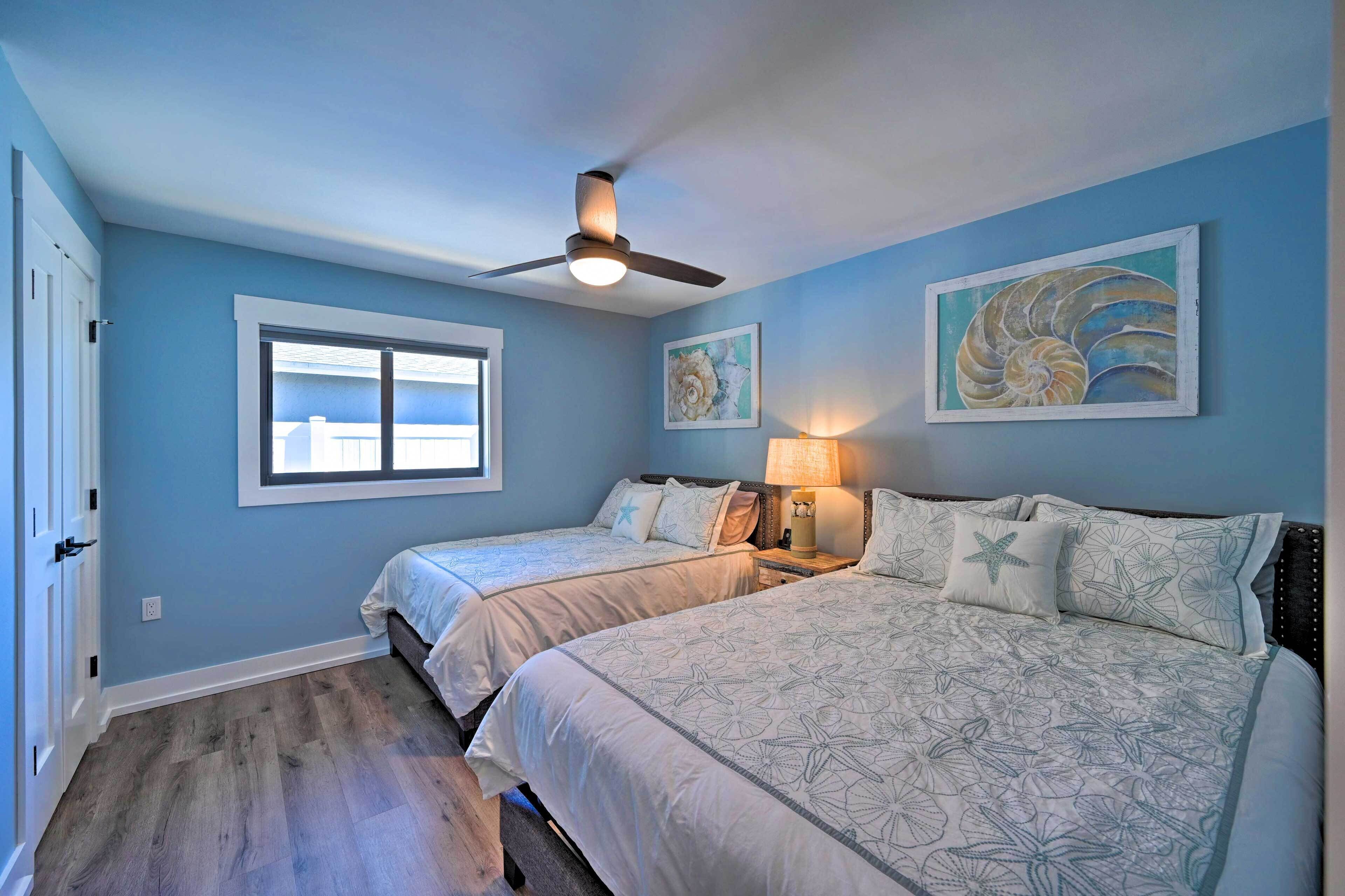 A bedroom with two beds, a ceiling fan, a window, and artwork on the walls.