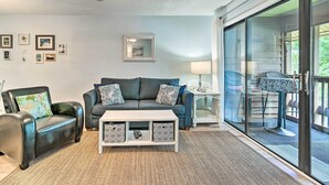 Un salon comprenant un canapé, un fauteuil, une table basse et une porte vitrée donnant sur un espace extérieur.
