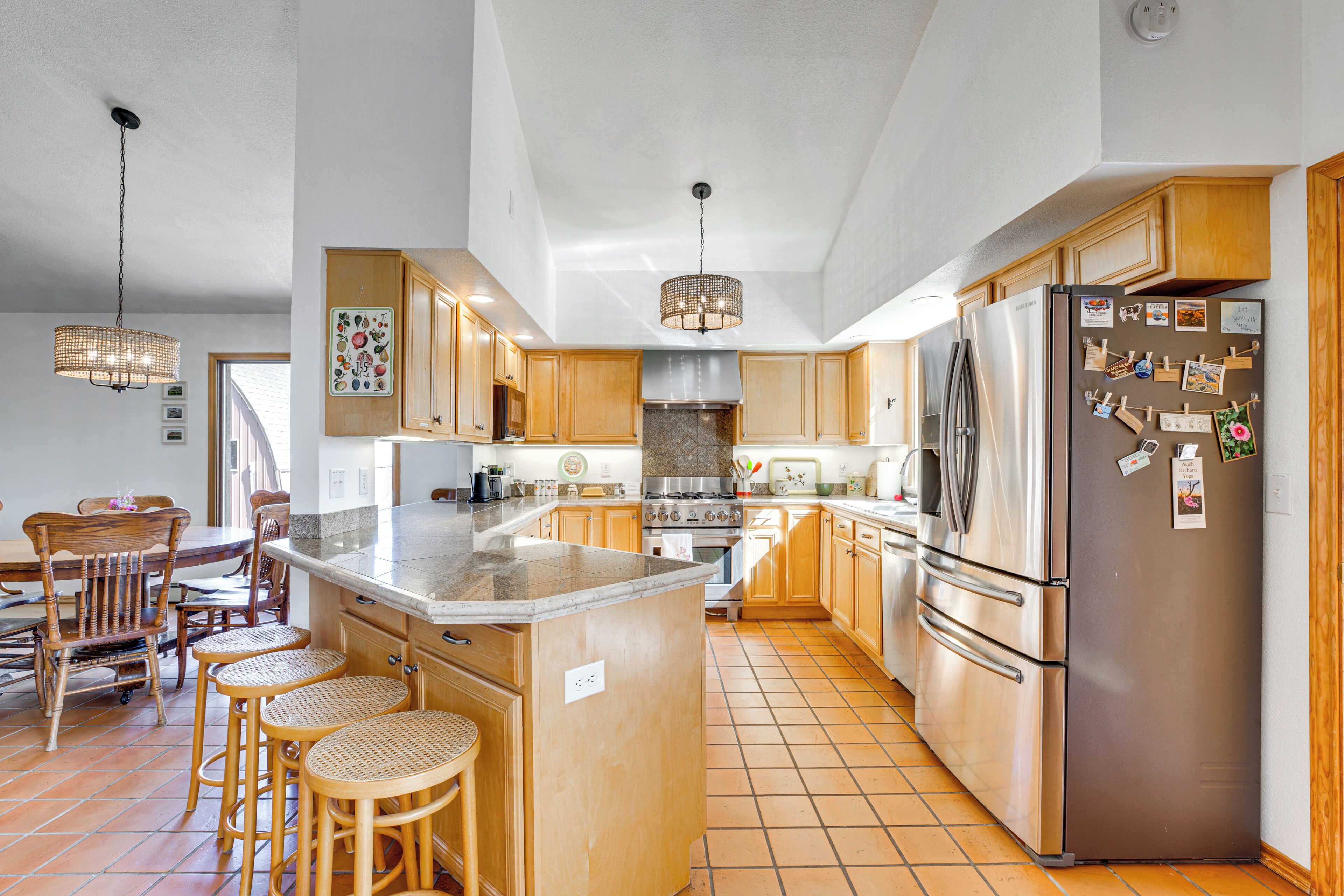 A modern kitchen with wooden cabinets, a stainless steel refrigerator, and a large island with stools.