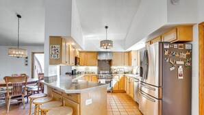 A modern kitchen with wooden cabinets, a stainless steel refrigerator, and a large island with stools. - 'mesa View House' w/ Hot Tub: Walk to Winery! (Palisade)