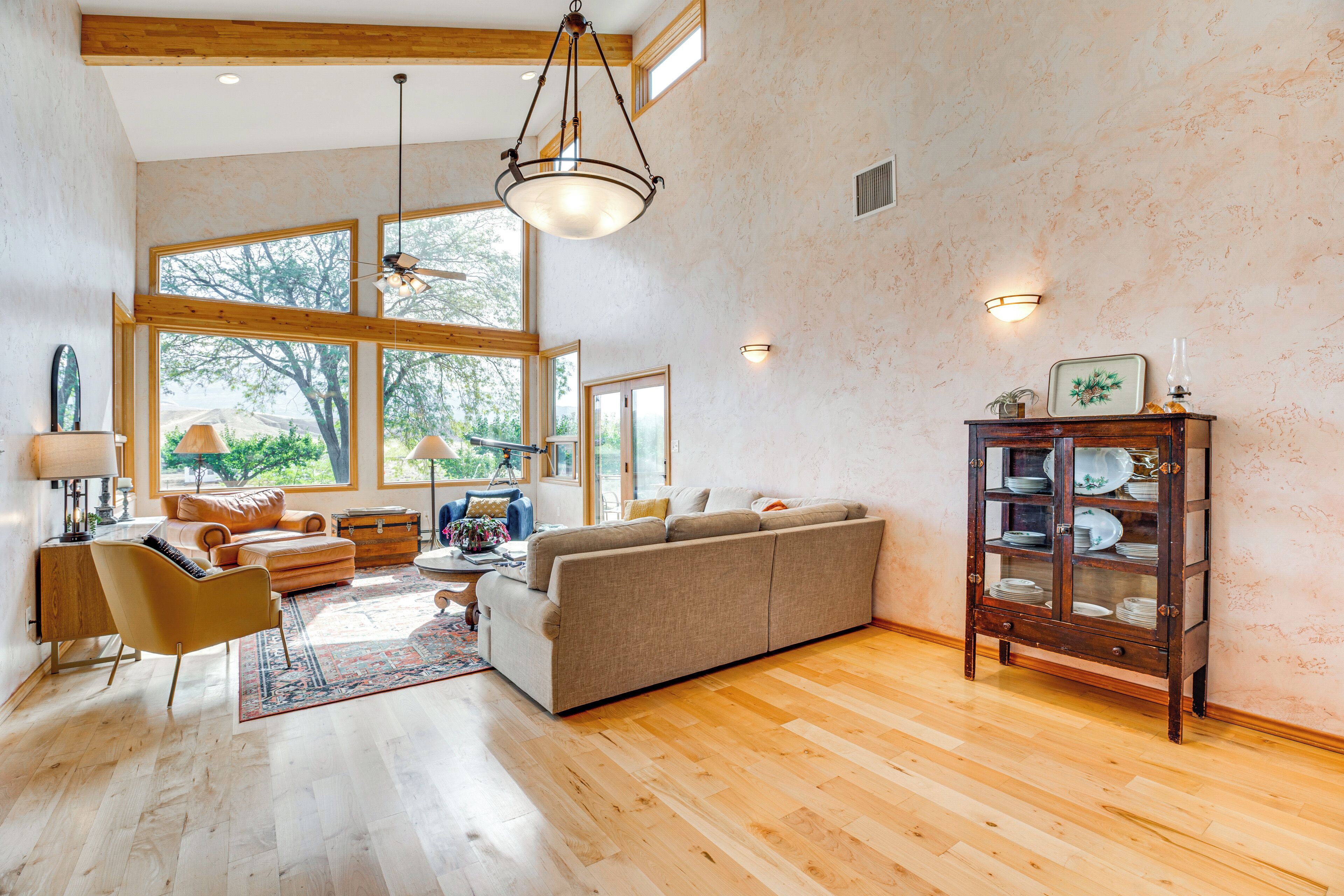 A spacious living room with a large sofa, wooden flooring, and a dining area with a cabinet.