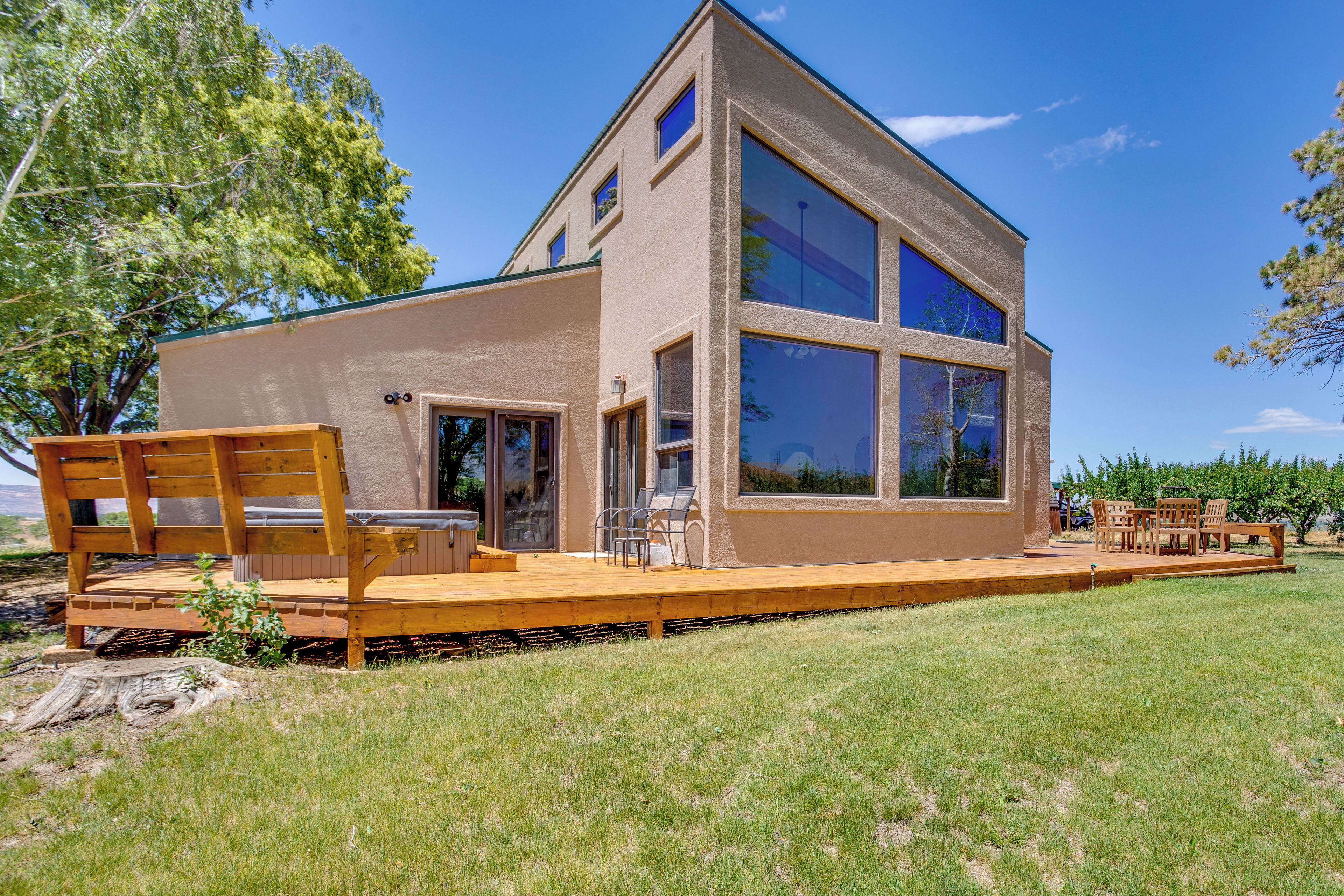 A modern two-story house with a large deck, outdoor seating, and a clear view of the surrounding landscape.