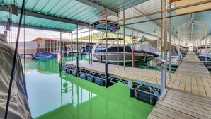 A covered marina with boats docked, a wooden deck, and a green pool area. - Beaver Lake Home w/ Game Room, Boat Slip & Views! (Eureka Springs)