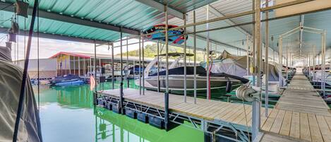 Ein überdachter Hafen mit vertäuten Booten, ein Holzdeck und ein Poolbereich mit Grünflächen.