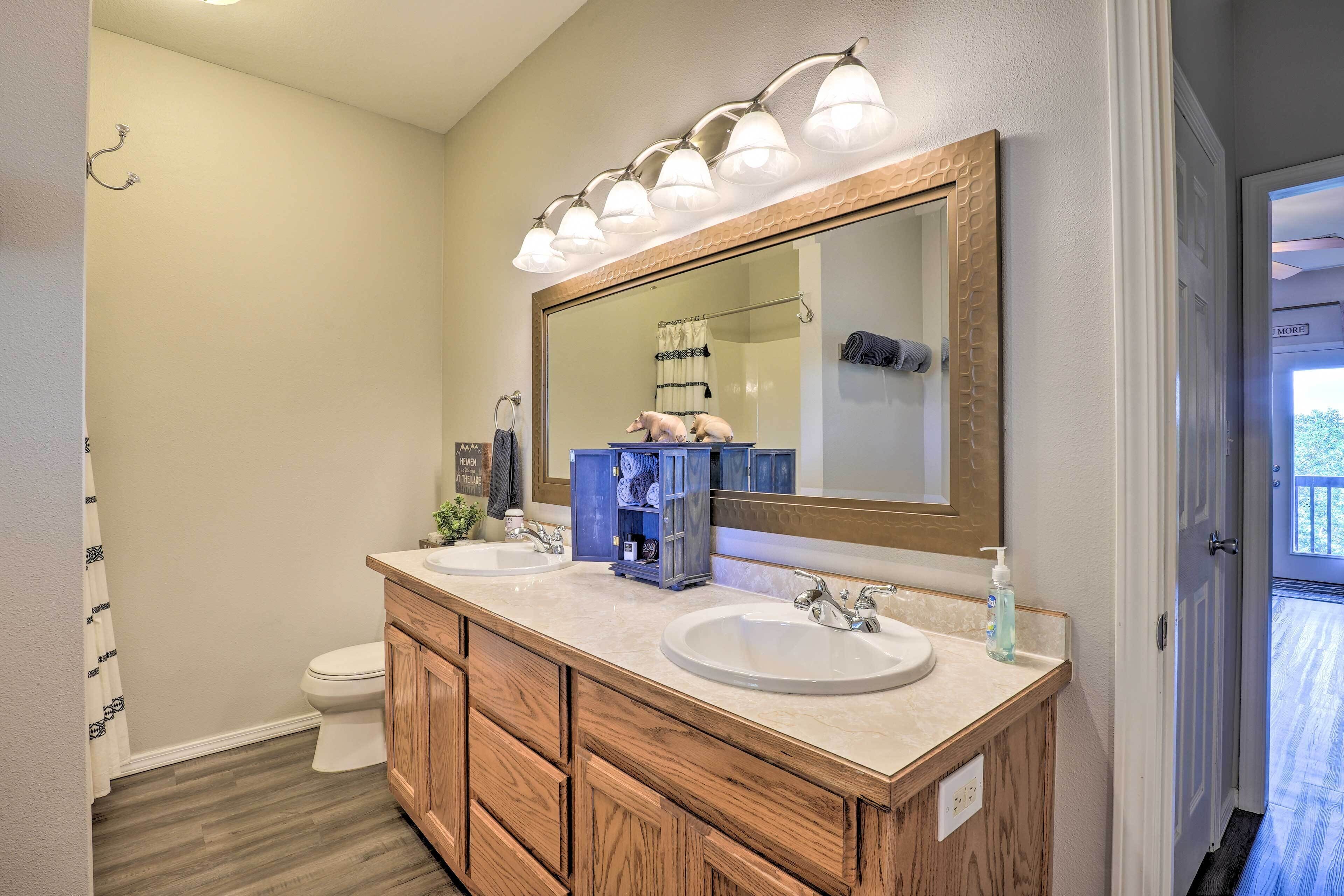 A bathroom with a wooden vanity, two sinks, a large mirror, and a shower curtain.